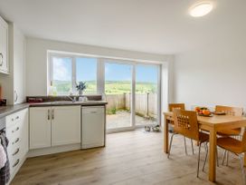 A kitchen with white cabinets wooden dining table and chairs and sliding glass door at 3 Tyn Y Mynydd in Penmachno