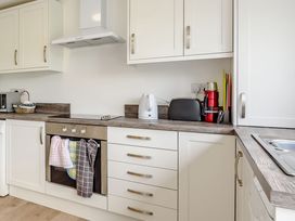 A kitchen with white cabinets a stovetop an oven with towels hanging on it a kettle toaster and utensils at 3 Tyn Y Mynydd in Penmachno