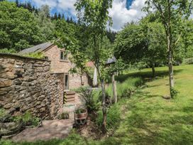 An outdoor view of a stone house surrounded by trees and grass at The Lodge Farm Barn Deepdean near Ross-on-Wye
