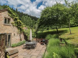 A garden with a stone patio, table, chairs, and trees at The Lodge Farm Barn Deepdean near Ross-on-Wye