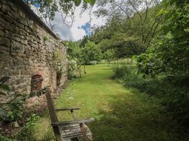A garden with a stone wall and a wooden chair at The Lodge Farm Barn Deepdean near Ross-on-Wye