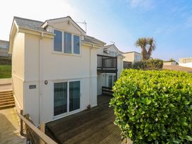 A view of cream colored houses with large windows and wooden decks surrounded by green shrubs at Beachcombers in Porth