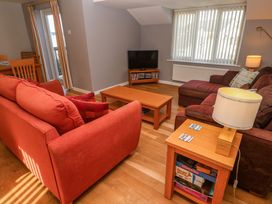 A living room with red and brown sofas a wooden coffee table a TV on a wooden stand and a lamp on a side table at Beachcombers in Porth