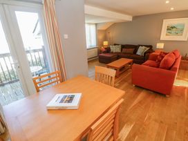A living room with a dining table and chairs a brown couch a red armchair wooden coffee tables lamps and a door to a balcony at Beachcombers in Porth