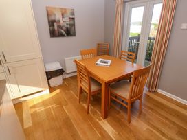 A dining area with a wooden table and four chairs next to glass doors and a trash bin at Beachcombers in Porth