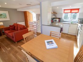 A dining area with wooden table and chairs next to a kitchen with white cabinets and a red blind at Beachcombers in Porth