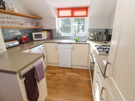 A kitchen with white cabinets wooden floor a window with orange blind and a countertop with appliances at Beachcombers in Porth