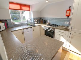 A kitchen with beige countertops white cabinets a gas stove oven a dishwasher and a window with a red blind at Beachcombers in Porth