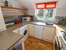 A kitchen with white cabinets a washing machine dishwasher microwave toaster and sink under a window at Beachcombers in Porth
