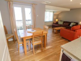 A dining area with a wooden table and chairs next to glass doors and a living area with sofas and a coffee table at Beachcombers in Porth