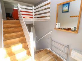 A wooden staircase with white railing next to a mirror and a wire shoe rack at Beachcombers in Porth