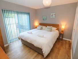 A bedroom with a double bed with white linens two rolled towels and pillows bedside tables with lamps and wall paintings at Beachcombers in Porth