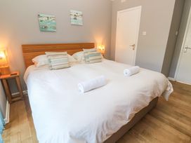 A bedroom with a large double bed two striped pillows two rolled white towels bedside tables with lamps and paintings on the wall at Beachcombers in Porth