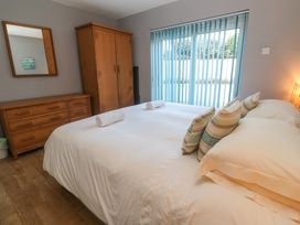 A bedroom with a bed and striped pillows wooden dresser and wardrobe near a window with blue vertical blinds at Beachcombers in Porth