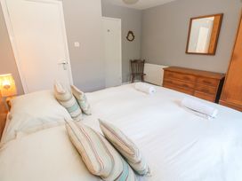 A bedroom with a double bed with pillows and rolled towels a wooden chair a wooden dresser with a mirror and a lamp on a bedside table at Beachcombers in Porth