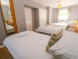 A bedroom with three single beds a window with curtains a door a closet and a standing mirror at Beachcombers in Porth