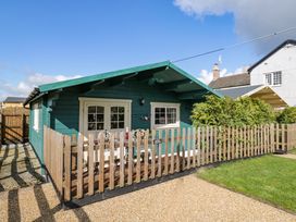 A small wooden cabin with green walls and cream window frames behind a wooden picket fence at The Nook in Royal Wootton Bassett