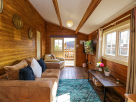 A living room with wooden walls a brown sofa an armchair a wall-mounted TV and a table with flowers at The Nook in Royal Wootton Bassett