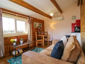 A living room with a beige sofa a wooden coffee table with flowers and plants a small dining table with chairs and a lamp at The Nook in Royal Wootton Bassett