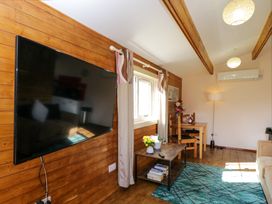 A living room with a mounted television flowers on a coffee table and a small dining table at The Nook in Royal Wootton Bassett