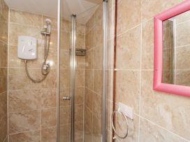 A shower area with beige tiled walls a white shower unit glass shower door a pink framed mirror and a towel ring in a bathroom at The Nook in Royal Wootton Bassett