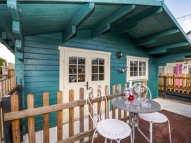 An outdoor patio with a small table and two chairs in front of a green wooden cabin at The Nook in Royal Wootton Bassett