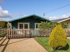 Exterior of a green wooden cabin with a fenced patio and nearby shrubs at The Nook in Royal Wootton Bassett