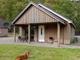 A wooden cottage with a patio table and chairs a barbecue and a dog lying on grass at Stone Water Cottage in Strathpeffer