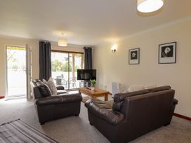 A living room with two brown leather sofas a wooden coffee table a television and sliding glass doors at Stone Water Cottage in Strathpeffer