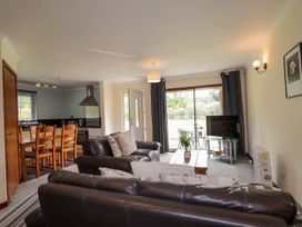 A living room with leather sofas a wooden dining table and chairs a kitchen area and a television near a sliding glass door at Stone Water Cottage in Strathpeffer