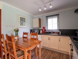 A kitchen with wooden dining table and chairs a wall clock microwave and window at Stone Water Cottage in Strathpeffer