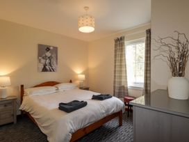 A bedroom with a wooden bed two bedside tables with lamps a window with plaid curtains and a dresser with a vase of twigs at Stone Water Cottage in Strathpeffer
