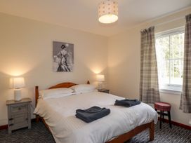 A bedroom with a double bed two bedside tables with lamps a window with curtains and a stool at Stone Water Cottage in Strathpeffer