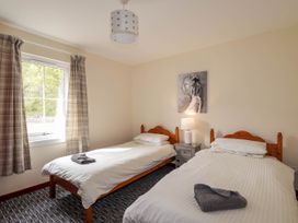 A bedroom with two single beds a nightstand with a lamp and a window with curtains at Stone Water Cottage in Strathpeffer