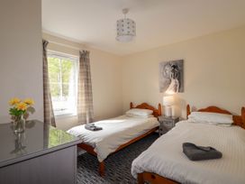 A bedroom with two single beds a bedside table with a lamp a window with curtains and a dresser with flowers at Stone Water Cottage in Strathpeffer