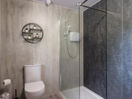 A bathroom with a toilet shower area with glass partition and wall-mounted shelf with small plants at Stone Water Cottage in Strathpeffer