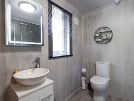 A bathroom with a toilet a sink a backlit mirror a window with blinds and a round wall shelf in Stone Water Cottage Strathpeffer