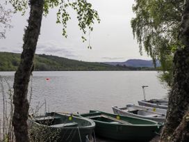 A lake with boats docked near the shore surrounded by trees and hills at Stone Water Cottage in Strathpeffer
