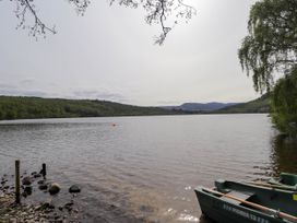 A lake with boats near a rocky shoreline and trees in the background at Stone Water Cottage in Strathpeffer
