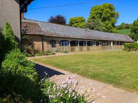 A long single story building with a slate roof and garden with flowers and picnic table at Keepers Cottage in Winterborne Stickland