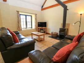 A living room with two black leather sofas red cushions a wood burning stove and a television at Keepers Cottage in Winterborne Stickland