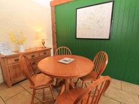 A dining area with a round wooden table and four wooden chairs next to a wooden cabinet with a lamp vase and guest book on it and a framed map on a green wall at Keepers Cottage in Winterborne Stickland