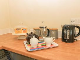A kitchen countertop with a kettle teapot sugar bowl milk jug French press storage containers and a cake stand with cake at Keepers Cottage in Winterborne Stickland