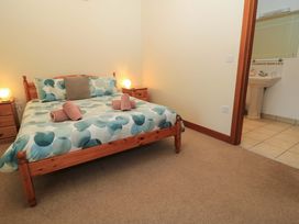 A bedroom with a wooden bed with patterned bedding two wooden bedside tables with lamps and an en suite bathroom with a sink at Keepers Cottage in Winterborne Stickland