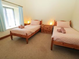 A bedroom with two single beds wooden furniture and a window with blue curtains at Keepers Cottage in Winterborne Stickland