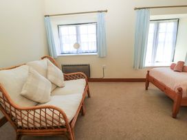 A room with a wooden framed sofa with cushions a wooden bed with towels and two windows with blue curtains at Keepers Cottage in Winterborne Stickland