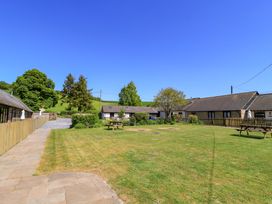 A large grassy yard with picnic tables stone walkway trees and cottages in the background at Keepers Cottage in Winterborne Stickland