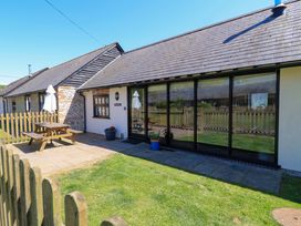 An exterior view of a cottage with a wooden picnic table and umbrella on a paved patio at New Barn in Winterborne Stickland
