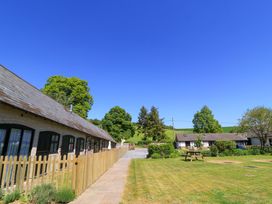 A grassy yard with a picnic table surrounded by buildings and trees at New Barn in Winterborne Stickland