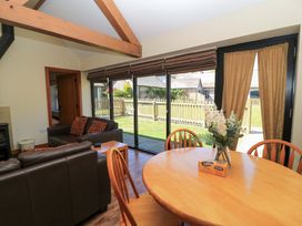 A living room with leather sofas, a wooden dining table with chairs, a vase with flowers, and large glass doors overlooking a garden at New Barn in Winterborne Stickland